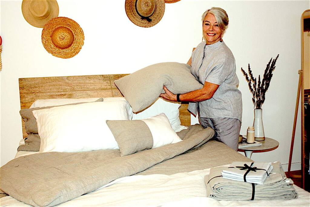 Rough Linen Founder Tricia Rose displays linen bedding and hand-sewn pillowslips, as well as a duvet cover, towels and curtains representing a few of the dozens of products her employees make. The list also includes tableware, runners, pinafores and her 'Touch' line of women's garments -- such as the boxy top she is modeling. (Gary Quackenbush Photo)