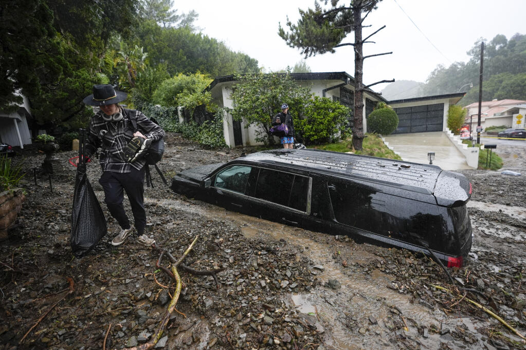 Residents evacuate past damaged vehicles after storms caused a mudslide, Monday, Feb. 5, 2024, in the Beverly Crest area of Los Angeles. A storm of historic proportions unleashed record levels of rain over parts of Los Angeles on Monday, endangering the city's large homeless population, sending mud and boulders down hillsides dotted with multimillion-dollar homes and knocking out power for more than a million people in California. (AP Photo/Marcio Jose Sanchez)