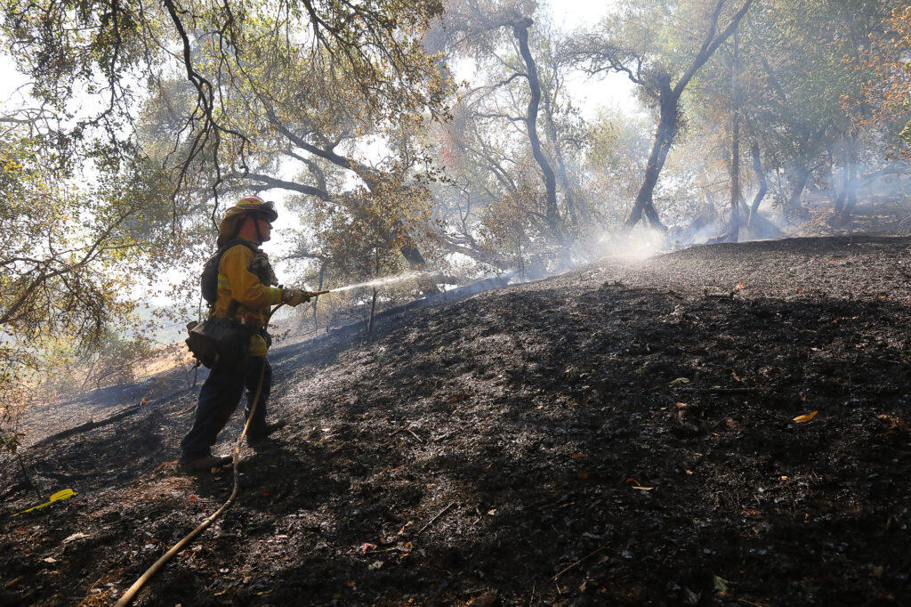 Rincon Valley Fire Department firefighter Neil Nicholson puts water on a hot spot while fighting a fire west of Westside Road, in Healdsburg on Thursday, August 16, 2018.  (Christopher Chung/ The Press Democrat)