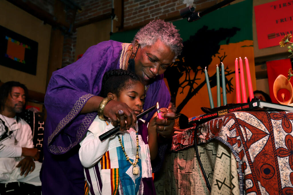 ReEllis Dotson-Newman, of Petaluma, helps her grandson, Ifetayo Newman-Grimsley, 3, visiting from Brooklyn, NY, as they light a candle in a ceremony honoring ancestors during the 3rd Annual NuBridges Kwanzaa celebration at the Arlene Francis Center, Saturday, Dec. 31, 2022, in Santa Rosa. (Darryl Bush / For The Press Democrat)