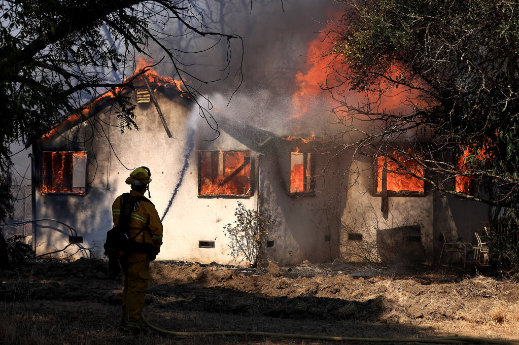 Firefighters take a defensive stand against a home burning on Forsythe Lane in Redwood Valley, ignited by an 80-acre wind-whipped brush fire, in tinder dry conditions, Wednesday, July 7, 2021.  (Kent Porter / The Press Democrat)