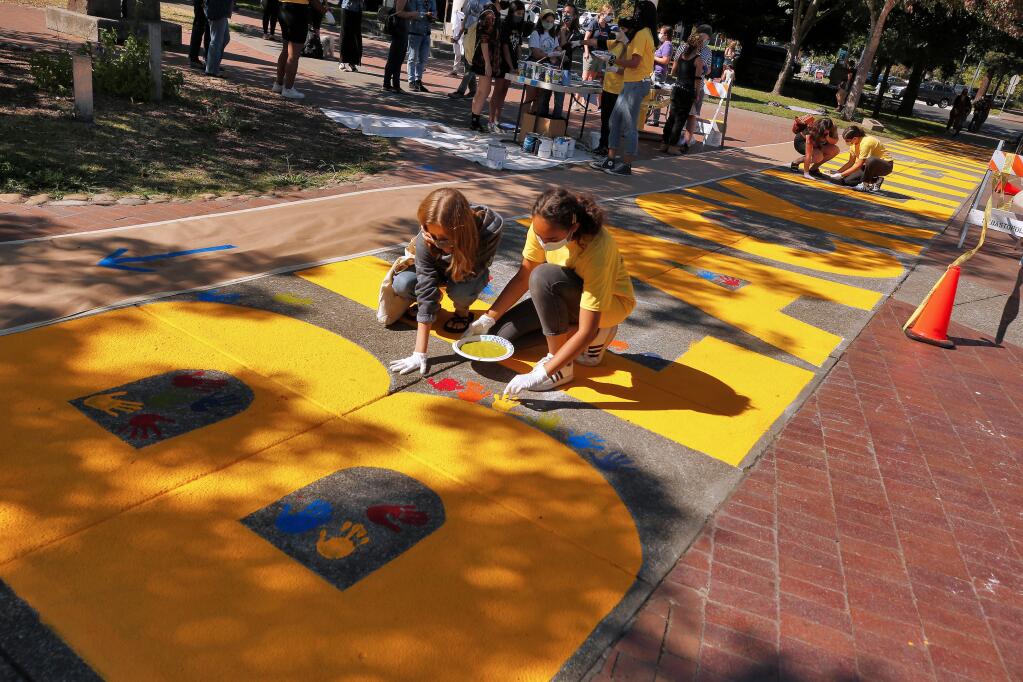 Zoe Reed, 17, left, of Sebastopol adds her handprint in paint to the Black Lives Matter painting at the town plaza with help from Adanna Okiwelu, 14, one of the coordinators of the painting, in Sebastopol, California, on Friday, July 24, 2020. (Alvin Jornada / The Press Democrat)