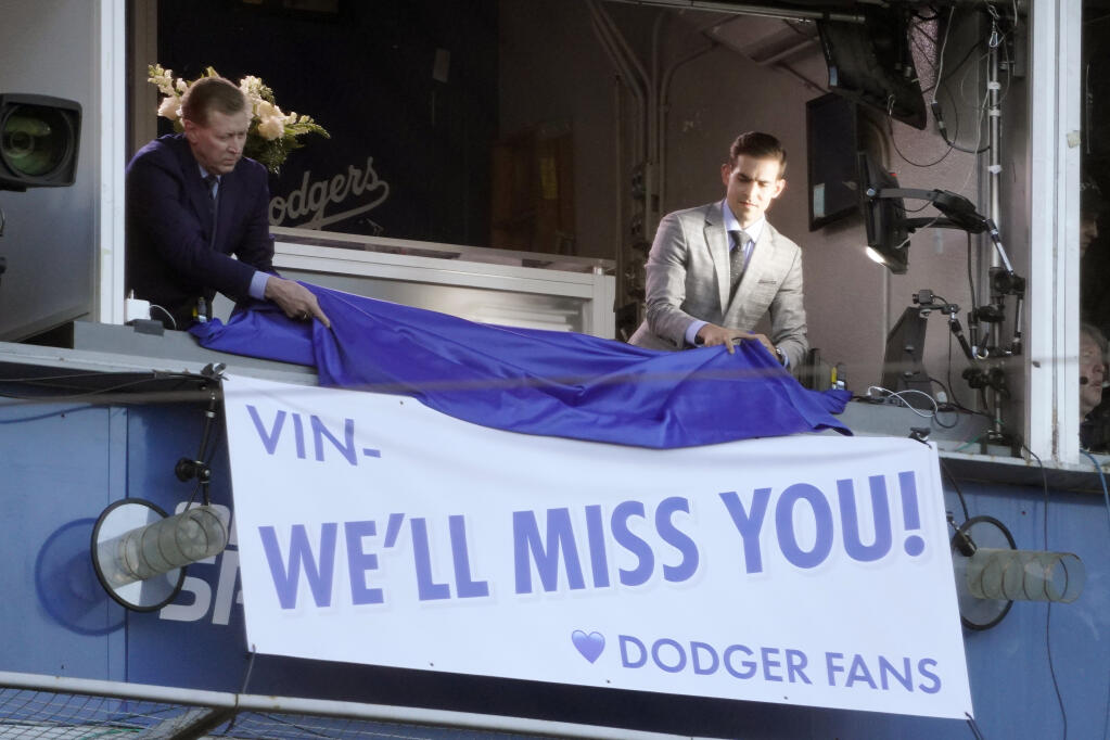 Broadcasters Orel Hershiser, left, and Joe Davis unveil a banner during a ceremony to honor the memory of Los Angeles Dodgers announcer Vin Scully prior to a baseball game between the Dodgers and the San Diego Padres Friday, Aug. 5, 2022, in Los Angeles. Scully, the Hall of Fame broadcaster, whose dulcet tones provided the soundtrack of summer while entertaining and informing Dodgers fans in Brooklyn and Los Angeles for 67 years, died Tuesday night. (AP Photo/Mark J. Terrill)