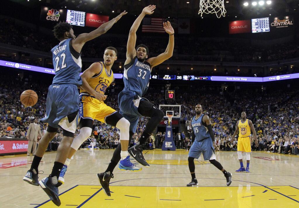 Golden State Warriors' Stephen Curry (30) makes a behind-the-back pass under the basket as Minnesota Timberwolves' Andrew Wiggins (22) and Karl-Anthony Towns (32) defend during the first half of an NBA basketball game Tuesday, April 5, 2016, in Oakland, Calif. (AP Photo/Marcio Jose Sanchez)