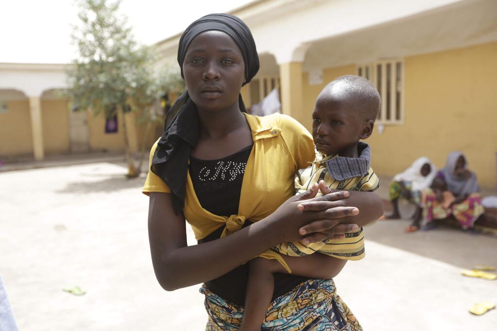FILE - In this Monday, May 4, 2015 file photo, Binta Ibrahim holds an unidentified child after she described told how at 16 she rescued three children aged between 2 and 4, cared for them during a year of captivity under Boko Haram and brought them to the safety of the refugee camp in Yola. All 275 women, girls and children rescued from Boko Haram and taken to the safety of a northeast Nigerian refugee camp have been taken into military custody amid suspicions that some are aiding the Islamic extremists, a camp official and a Nigerian military intelligence officer said Wednesday May 20, 2015. (AP Photo/Sunday Alamba, File)