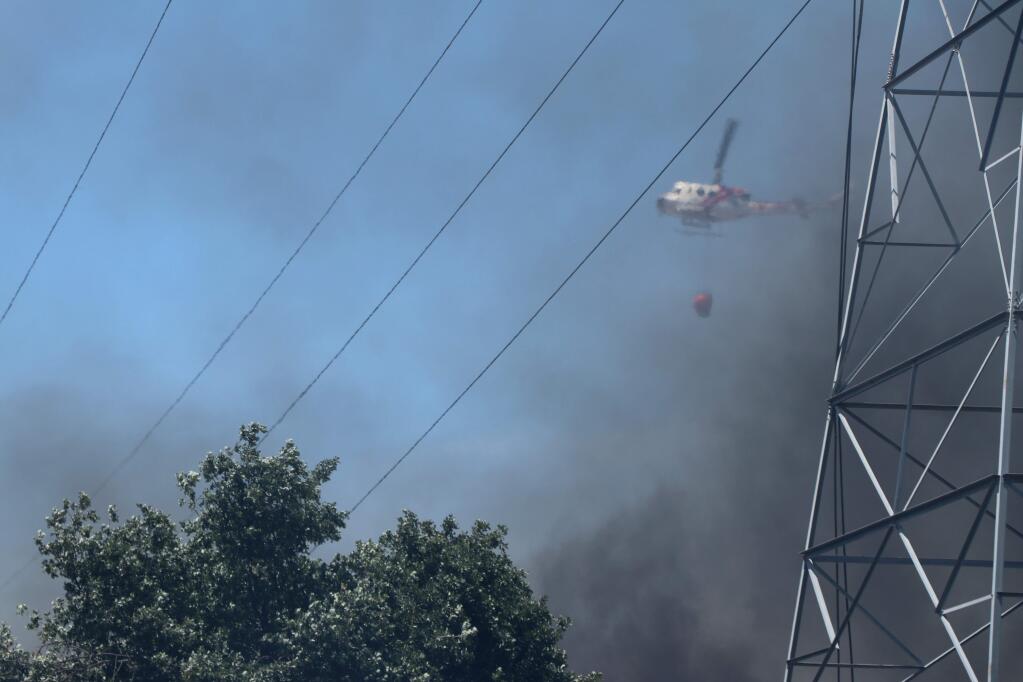 A Cal Fire helicopter brings water to a fire at a pallet factory in Schellville, near Sonoma, flying over a PG&E power line that suffered damage in the fire. (Christian Kallen/Index-Tribune)