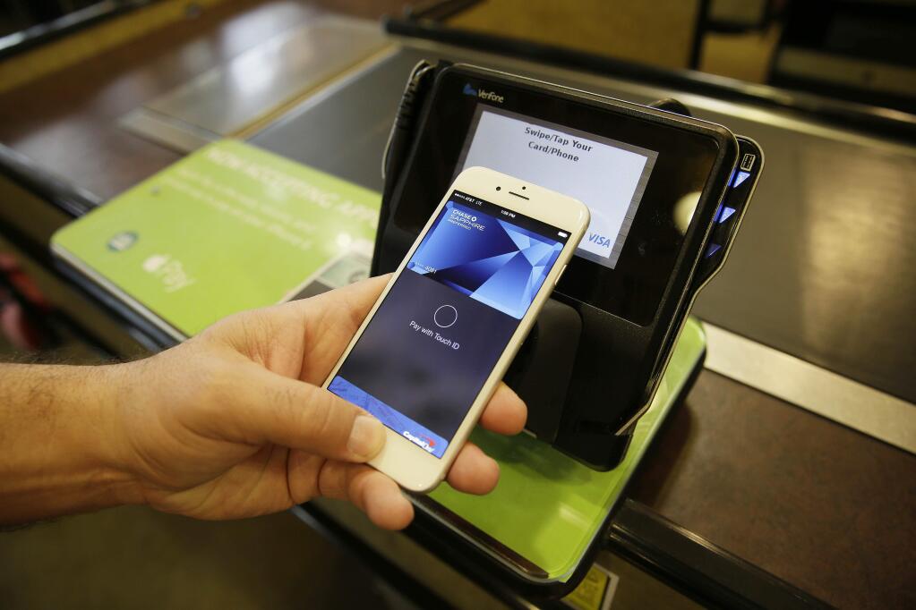 In this photo taken Friday, Oct. 17, 2014, Eddy Cue, Apple Senior Vice President of Internet Software and Services, demonstrates the new Apple Pay mobile payment system at a Whole Foods store in Cupertino, Calif. (AP Photo/Eric Risberg)