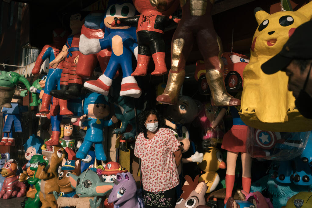 Maricela Ortega among the piñatas at her husband's piñata shop in Mexico City, on March 31, 2021. The piñata industry, dependent on social gatherings, has seen sales plummet. Some artisans, in a creative bid to survive, have added coronavirus figures to their lineups of superheros and princesses. (Luis Antonio Rojas/The New York Times)