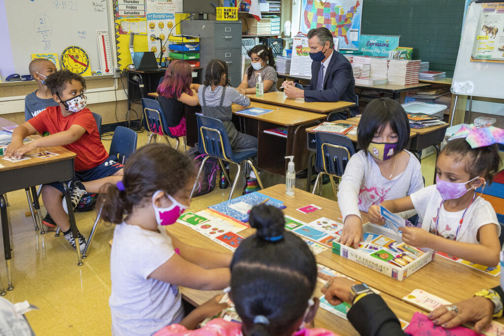 California Gov. Gavin Newsom sits with students of a second grade classroom at Carl B. Munck Elementary School, Wednesday, Aug. 11, 2021, in Oakland, Calif. Gov. Newsom announced that California will require its 320,000 teachers and school employees to be vaccinated against the novel coronavirus or submit to weekly COVID-19 testing. The statewide vaccine mandate for K-12 educators comes as schools return from summer break amid growing concerns of the highly contagious delta variant. (Santiago Mejia/San Francisco Chronicle via AP, Pool)