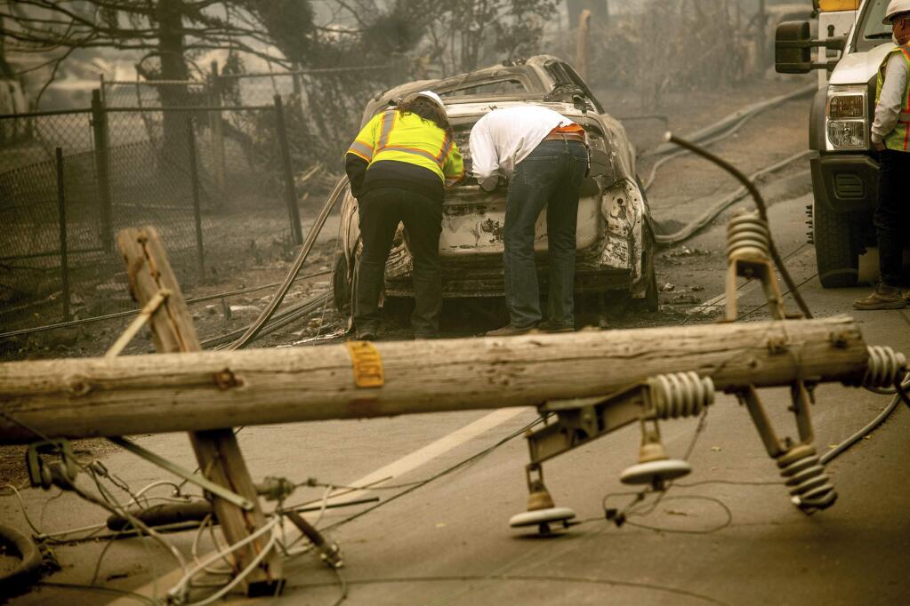 FILE - In this Nov. 10, 2018 file photo, with a downed power utility pole in the foreground, Eric England, right, searches through a friend's vehicle after the wildfire burned through Paradise, Calif. Pacific Gas & Electric Corp. is expected to file for bankruptcy protection Tuesday, Jan. 29, 2019. (AP Photo/Noah Berger, File)