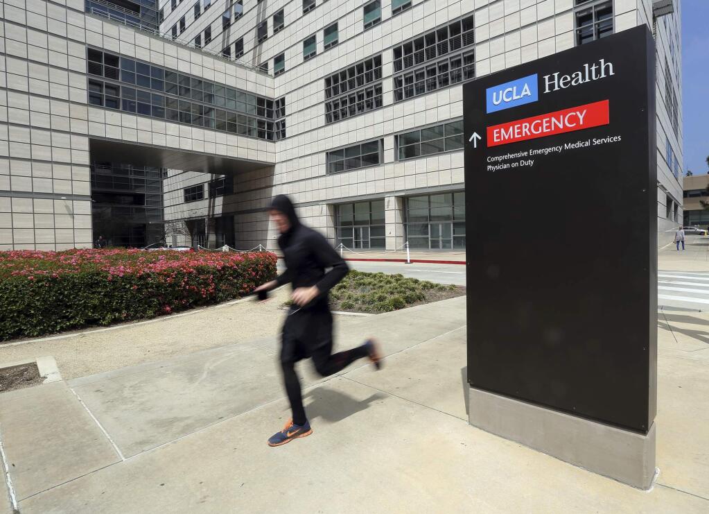 FILE - In this April 26, 2019, file photo, a runner passes the Ronald Reagan UCLA Medical Center on the campus of the University of California, Los Angeles. A woman says she was sexually assaulted by a gynecologist who worked for the University of California, Los Angeles and is upset the school apparently knew about it from her social media post but never contacted her as it investigated other incidents that led to criminal charges. (AP Photo/Reed Saxon, File)