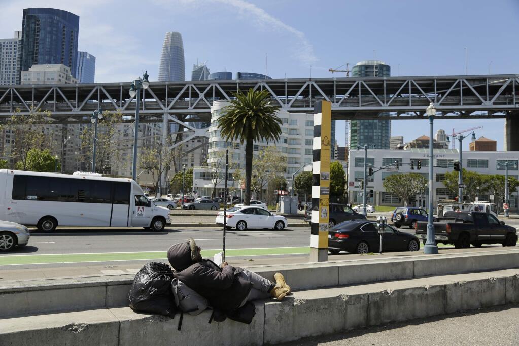 In this Thursday, April 18, 2019 photo, a man rests and reads the Bible while sitting across the street from the proposed site of a homeless shelter in San Francisco. The city of San Francisco, which has too little housing and too many homeless people sleeping in the streets, is teeming with anxiety and vitriol these days. A large new homeless shelter is on track to go up along a scenic waterfront area dotted with high-rise luxury condos, prompting outrage from some residents. (AP Photo/Eric Risberg)