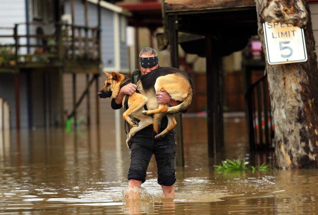 Jeremiah Dock carries his dog, Sergeant , from his home in the Sycamore Court Apartments on Church St. as the Russian River crested in Guerneville on Monday morning, January 9, 2017. (John Burgess/The Press Democrat)