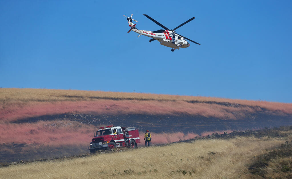 Rancho Adobe Fire District personnel work on mopping up the Roblar Fire as a Cal Fire helicopter flies overhead near Hessel on Monday, June 27, 2022.  (Christopher Chung/The Press Democrat)