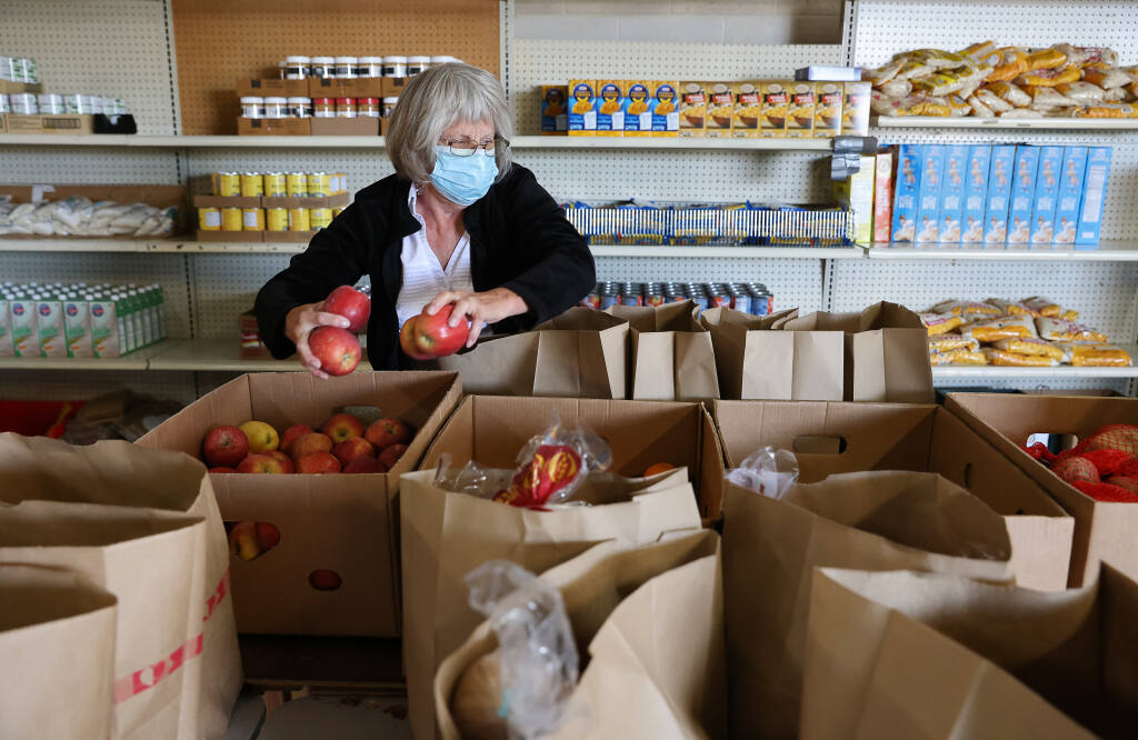 Volunteer Beverly Schaap places apples into bags of groceries to be given to people in need at F.I.S.H. of Santa Rosa on Thursday, April 28, 2022.  (Christopher Chung/ The Press Democrat)