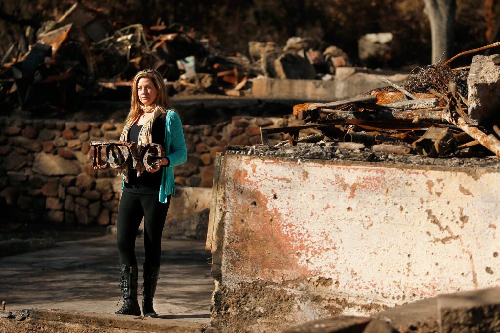 Visual artist Helena Donzelli poses for a portrait where her former home and studio burned during the Nuns fire in Glen Ellen, California on Friday, December 29, 2017. The burned piece of metalwork she holds is one of the salvaged items she has been commissioned to create new artwork from, by clients who lost their homes and other belongings in the October fires. (Alvin Jornada / The Press Democrat)