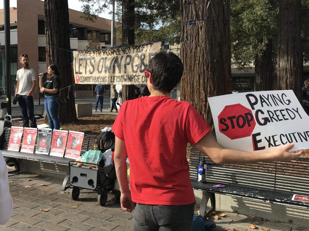 Russ Aguilar, right, holds a sign critical of PG&E while Alba Diaz translates J.D. Opperman's remarks into Spanish at a rally organized by the North Bay chapter of the Democratic Socialists of America on Saturday, Nov. 16, 2019, at Old Courthouse Square in Santa Rosa. (Will Schmitt/The Press Democrat)