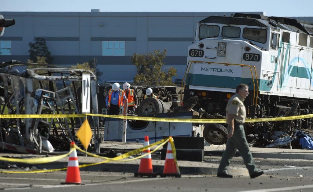 Workers walk next to a Metrolink train that hit a truck and then derailed, Tuesday, Feb. 24, 2015, in Oxnard, Calif. Three cars of the Metrolink train tumbled onto their sides, injuring dozens of people in the town 65 miles northwest of Los Angeles. (AP Photo/Mark J. Terrill)