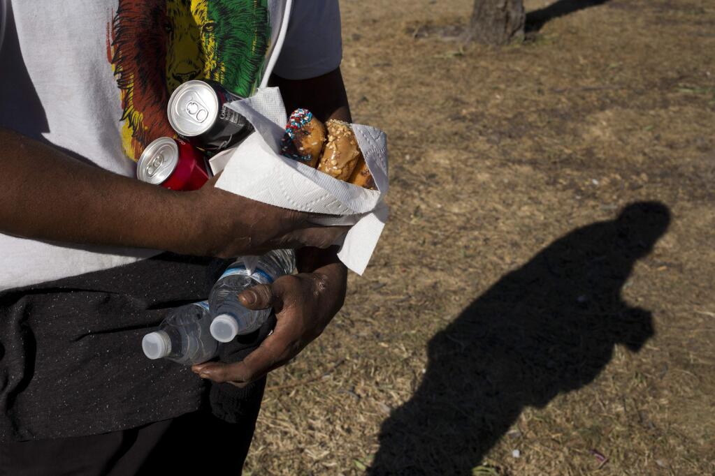 Homeless Jonathan Young, 40, carries donuts, soda and two bottles of water donated to him by church members in a homeless encampment set up on the Santa Ana River trail Saturday, Dec. 9, 2017, in Anaheim, Calif. Goodhearted neighbors heartbroken over the rising number of homeless in their communities are dishing out hot meals, providing mobile showers and handing out sandwiches to those in need. But some question whether they're doing more harm than good. (AP Photo/Jae C. Hong)
