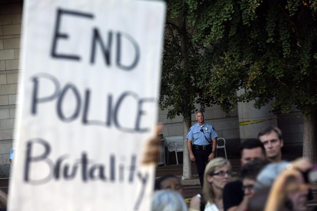 A member of the Clayton police department stands watch as protesters gather outside the Buzz Westfall Justice Center, Wednesday, Aug. 20, 2014, in Clayton, Mo. A grand jury has begun hearing evidence as it weighs possible charges against the Ferguson police officer who fatally shot 18-year-old Michael Brown. (AP Photo/Jeff Roberson)