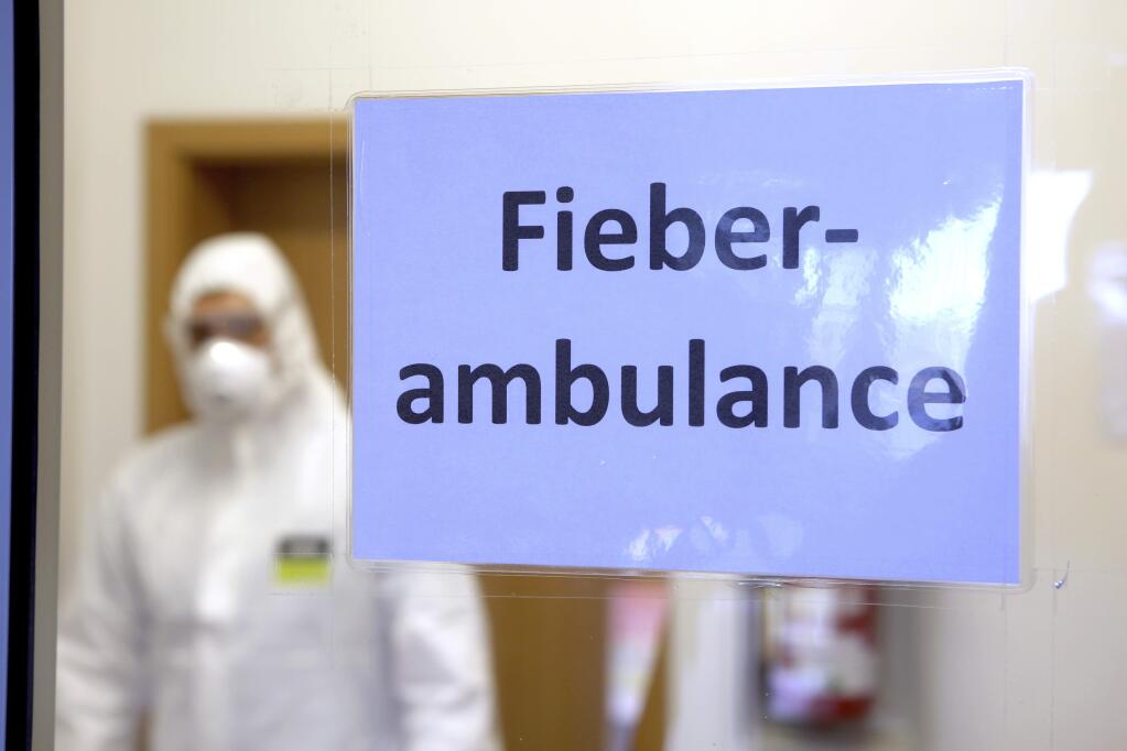 A person in protective gear stands behind a sign reading 'Feaver Ambulance' in the reception area of the fever outpatient clinic in Wernigerode, Germany, Monday, March 16, 2020. For most people, the new coronavirus causes only mild or moderate symptoms, such as fever and cough. For some, especially older adults and people with existing health problems, it can cause more severe illness, including pneumonia. (Matthias Bein/dpa via AP)