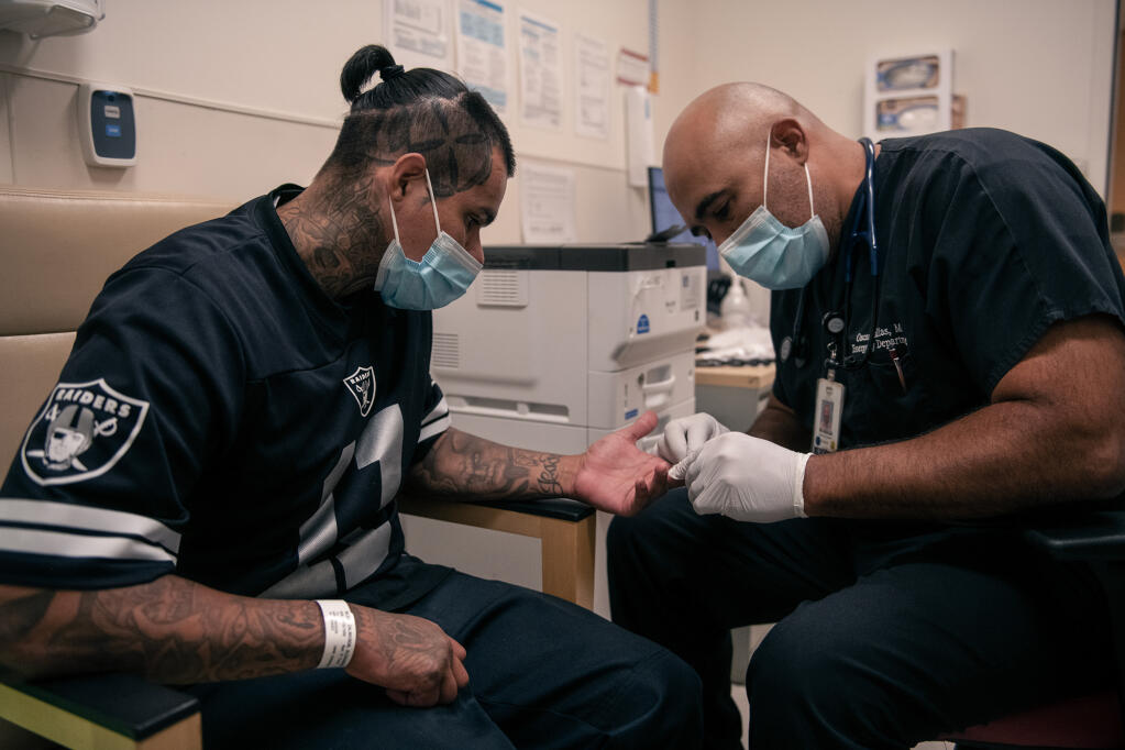 Dr. Oscar Casillas removes a pair of stitches from Alex’s hand at Martin Luther King Jr. Community Hospital on July 26, 2022. Photo by Pablo Unzueta for CalMatters