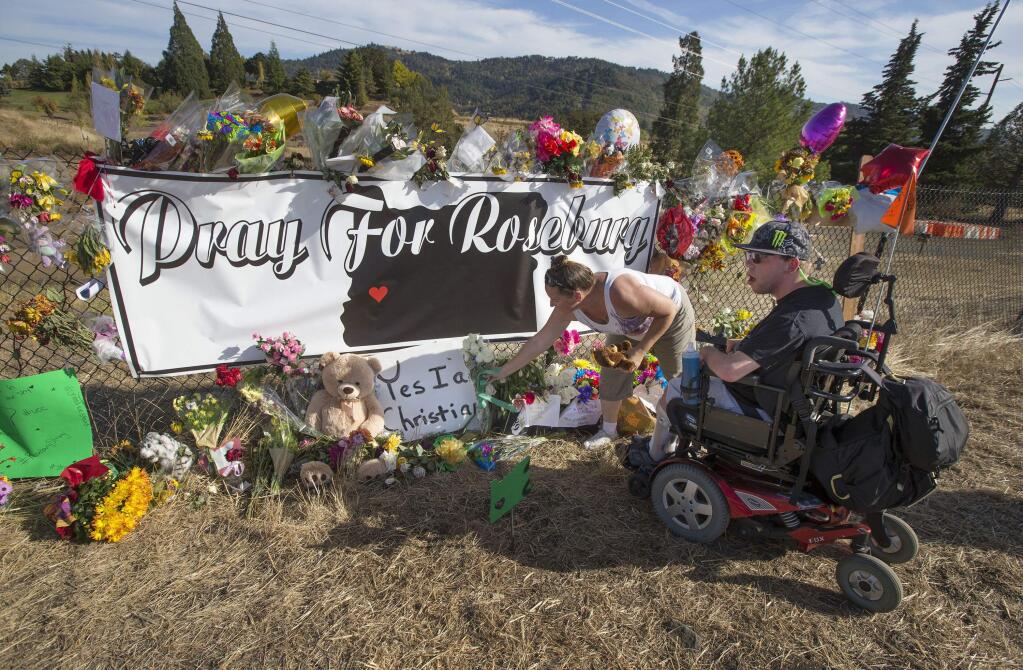 Candida Miller, left, and Brandon Snyder leave flowers at a site of a growing memorial to victims of the mass shooting at Umpqua Community College in Roseburg, Ore., Tuesday, Oct. 6, 2015. (AP Photo via Chris Pietsch/The Register-Guard)