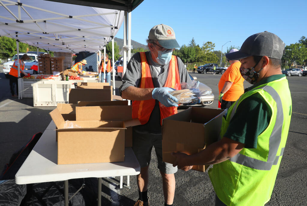 Robert Bauer, left, with the Cloverdale Senior Center, packs a food box with Yovani Enriquez while volunteering with the Redwood Empire Food Bank distribution at the Cloverdale Citrus Fairgrounds on Monday, Oct. 26, 2020. (Christopher Chung / The Press Democrat)