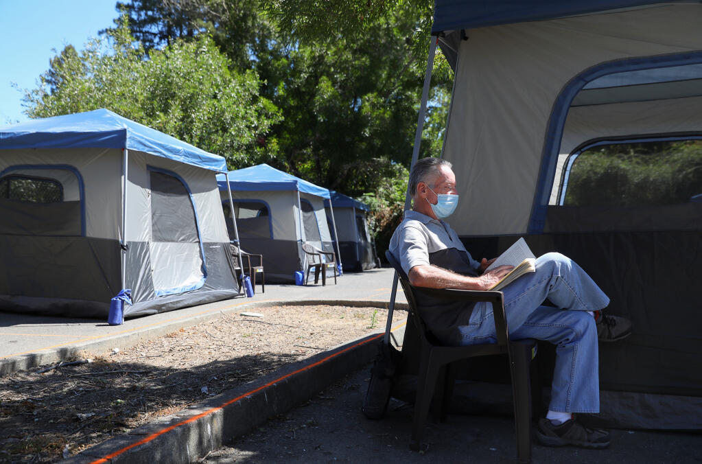 Brian Fielding reads outside of his tent at the newest Sonoma County-provided encampment for homeless individuals in Guerneville on Wednesday, Aug. 12, 2020.  (Christopher Chung / The Press Democrat)