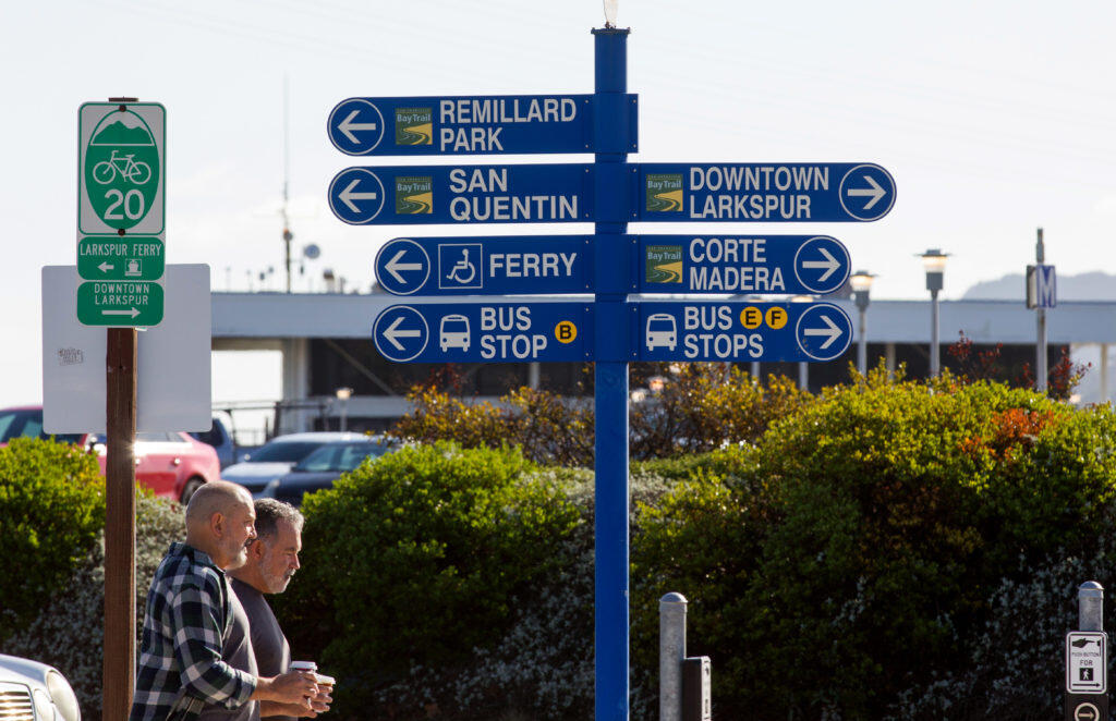 People walk near signs near a cross walk on Sir Francis Drake Blvd., that is between the newly opened Larkspur SMART Train Station and the Larkspur Ferry Terminal, in Larkspur, Calif., on Saturday, December 14, 2019. (Photo by Darryl Bush / For The Press Democrat)