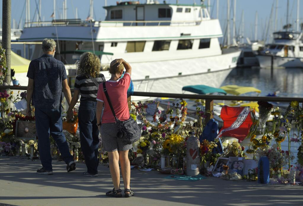 FILE - In this Sept. 6, 2019 file photo people visit a growing memorial to the victims who died aboard the dive boat Conception as its sister boat Vision sits in the background, in Santa Barbara, Calif. The owner of the scuba diving boat company has announced an indefinite suspension of its fleet in the wake of the fatal boat fire off the Southern California coast that killed 34 people. Truth Aquatics Inc. says Tuesday, Oct. 1, 2019 on its Facebook page that the company will 'dedicate our entire efforts to make our boats models of new regulations' in collaboration with the Coast Guard and the National Transportation Safety Board. (AP Photo/Mark J. Terrill,File)