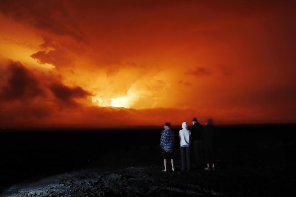 People watch the eruption of Mauna Loa, Monday, Nov. 28, 2022, near Hilo, Hawaii. Mauna Loa, the world's largest active volcano erupted Monday for the first time in 38 years. (AP Photo/Marco Garcia)