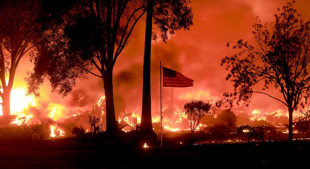 An American flag whips in the wind as structures burn in Coffey Park, Monday Oct. 9, 2017 at Randon Way and Hopper Lane . (Kent Porter / The Press Democrat)