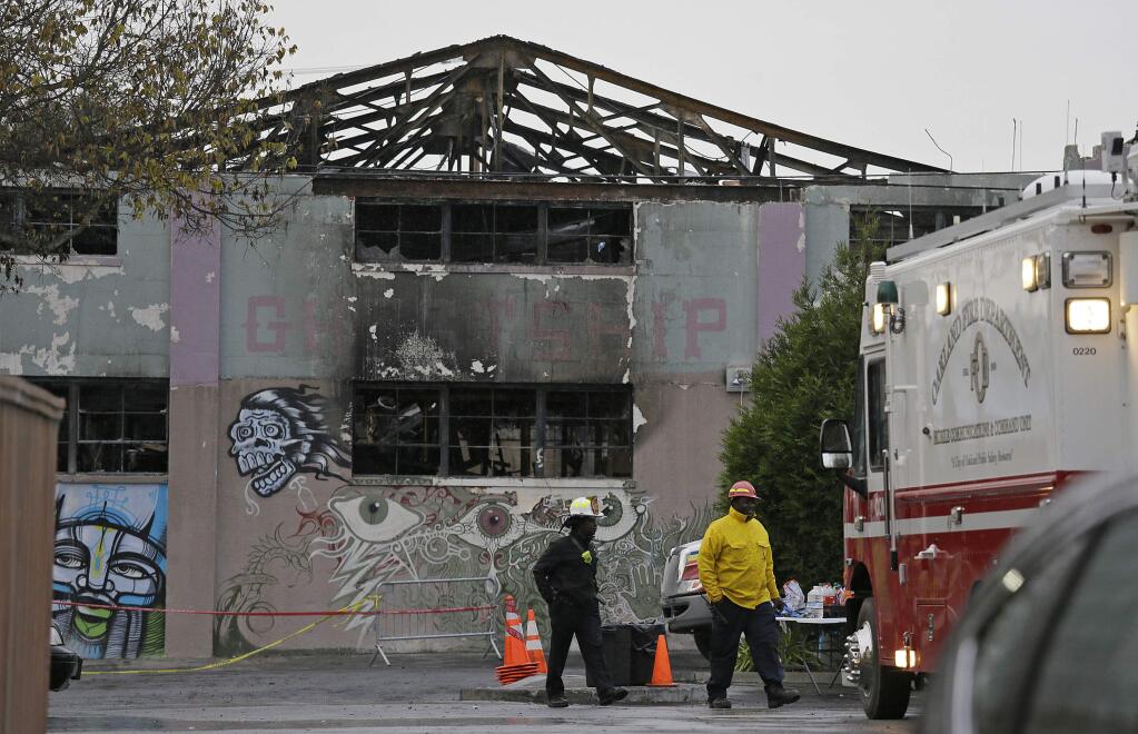 FILE - In this Dec. 7, 2016 file photo, Oakland fire officials walk past the remains of the Ghost Ship warehouse damaged from a deadly fire in Oakland, Calif. Two men who pleaded no contest to 36 charges of involuntary manslaughter will face the family members of those who died in a fire at an illegally converted Northern California warehouse. A two-day sentencing hearing for Derick Almena and Max Harris is scheduled to begin Thursday, Aug. 9, 2018, in Oakland. (AP Photo/Eric Risberg, File)