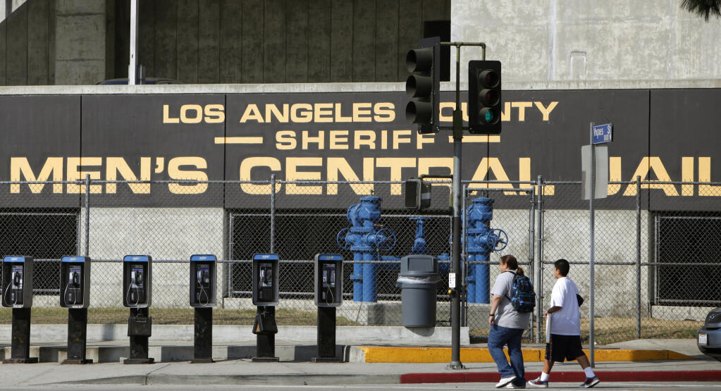 FILE - In this Sept. 28, 2011 photo, people walk past the Los Angeles County Sheriff's Men's Central Jail facility in Los Angeles. Up to one-third of the 12,000 inmates in Los Angeles County jails can’t get to their court appearances because of a shortage of functioning buses, and county supervisors this week advanced a proposal to try and fix the problem. (AP Photo/Damian Dovarganes, File)