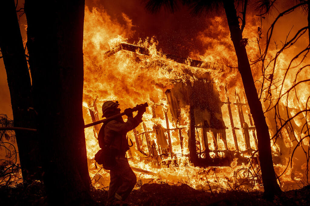 As wildfires intensify, thousands of overworked California firefighters carry a heavy load of trauma, pain and grief. Here, firefighter Jose Corona sprays water as flames from the Camp Fire consume a home in Magalia on Nov. 9, 2018. Photo by Noah Berger, AP Photo