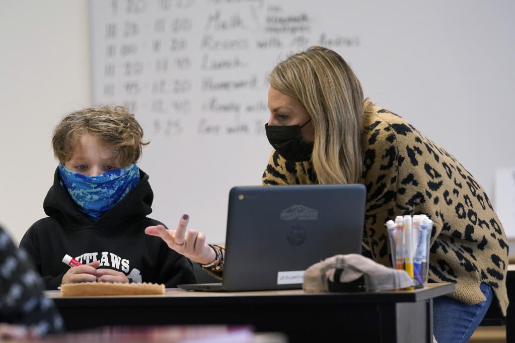 Teacher Lisa Tyler, right, wears a mask as she works with Gabriel Worthey, 10, on a math problem in a fourth-grade classroom, Tuesday, Feb. 2, 2021, at Elk Ridge Elementary School in Buckley, Wash. (AP Photo/Ted S. Warren)