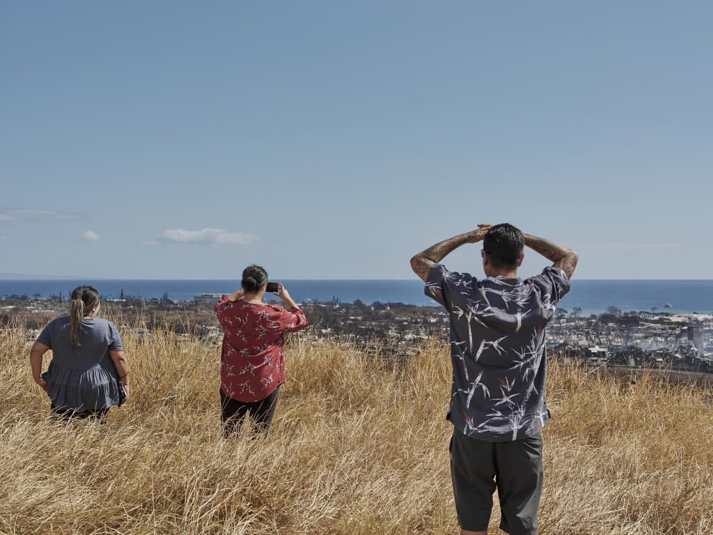 People look at the destruction of Lahaina due to wildfires in Lahaina, Hawaii, Aug. 11, 2023. A sweeping series of plantation closures in Hawaii allowed highly flammable nonnative grasses to spread on idled lands, providing the fuel for huge blazes. (Philip Cheung/The New York Times)