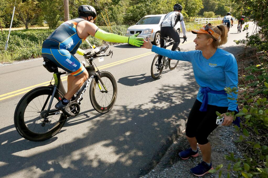 Olga Fernandez, right, of Windsor encourages triathletes as they pedal up Faught Road, while she waits to cheer on her friend who is also competing in the race, during the cycling stage of Ironman Santa Rosa in Windsor, California, on Saturday, May 11, 2019. (Alvin Jornada / The Press Democrat)