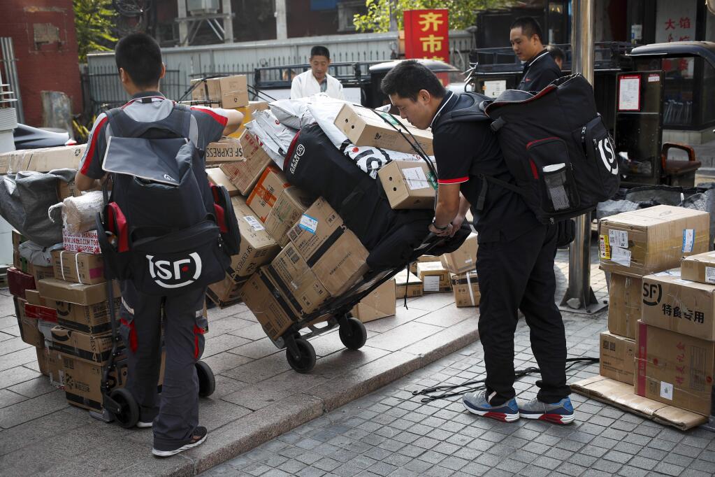 Delivery workers pull carts loaded boxes of goods for their customers outside an office building in Beijing, Monday, Sept. 10, 2018. China on Monday promised retaliation if U.S. President Donald Trump escalates their tariff battle, raising the risk Beijing might target operations of American companies as it runs out of imports for penalties. (AP Photo/Andy Wong)