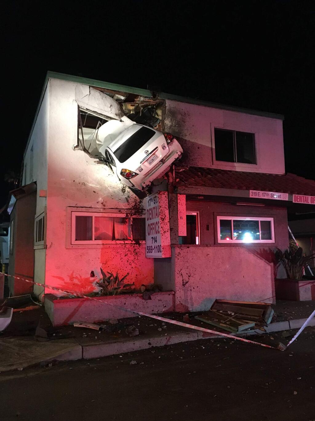 In this Sunday, Jan. 14, 2018, photo provided by Orange County Fire Authority, a vehicle that crashed into a building hangs from a second story window in Santa Ana, Calif. Members from Orange County Fire Authority and Los Angeles County Urban Search & Rescue rescued two people, who escaped serious injuries when the car they were in went airborne and slammed into the second floor of a dental office in Southern California. Authorities say the Nissan Altima hit a center divider early Sunday, soared into the air and plowed into the top floor of the two-story structure. (Capt. Stephen Horner /Orange County Fire Authority via AP)