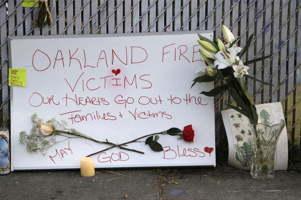FILE - In this Dec. 5, 2016 file photo, signs and flowers adorn a fence near the site of a warehouse fire in Oakland, Calif. (AP Photo/Marcio Jose Sanchez, File)