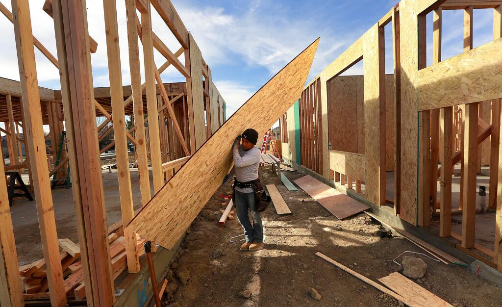 Carlos Tapia lifts siding onto a home at Aria Place, a 55-unit project in northwest Santa Rosa. (JOHN BURGESS / The Press Democrat)