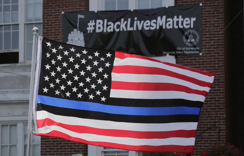 FILE - In this July 28, 2016, file photo, a flag with a blue and black stripes in support of law enforcement officers, flies at a protest by police and their supporters outside Somerville City Hall in Somerville, Mass. San Francisco's police chief said the city's rank and file will wear neutral face coverings to defuse a controversy that was sparked when officers sent to patrol a May Day protest wore masks adorned with the 'thin blue line' flag. (AP Photo/Charles Krupa, File)