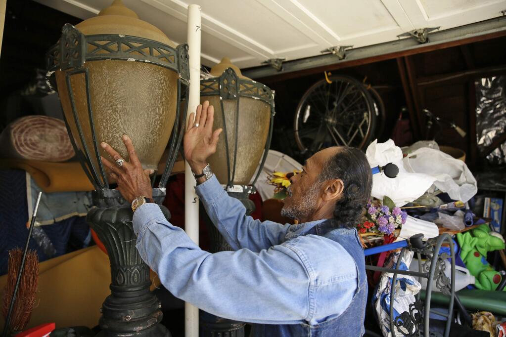 In this Thursday, June 22, 2017, photo, Graciano de la Cruz adjusts the top of an historic streetlamp he will need to try and sell in the garage of his home in San Francisco. La Cruz grew up in San Francisco, the child of a Filipino father and an African-American mother. He and his wife, Buena, who is Filipino-American, must now sell their own home of two decades to pay off a debt that stemmed from a 'pick-a-payment' loan with World Savings Bank in August 2006. (AP Photo/Eric Risberg)