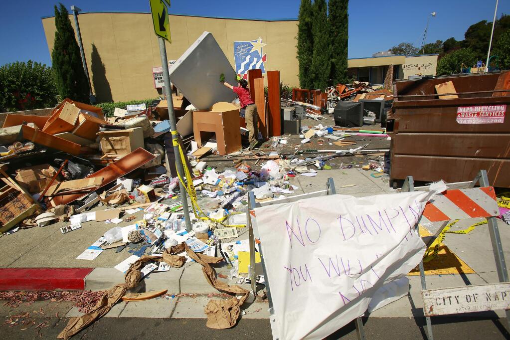 A man dumps a mattress in with a large pile of trash created from Sunday's earthquake in front of Browns Valley Elementary School in Napa on Tuesday, August 26, 2014. (Conner Jay/The Press Democrat)