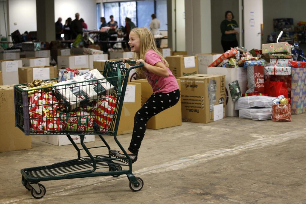 Volunteer Amelia Laird, 9, rides the shopping cart as she helps sort Giving Tree gifts for children and adults in need at a warehouse in Santa Rosa, on Tuesday, December 22, 2015. (BETH SCHLANKER/ The Press Democrat)
