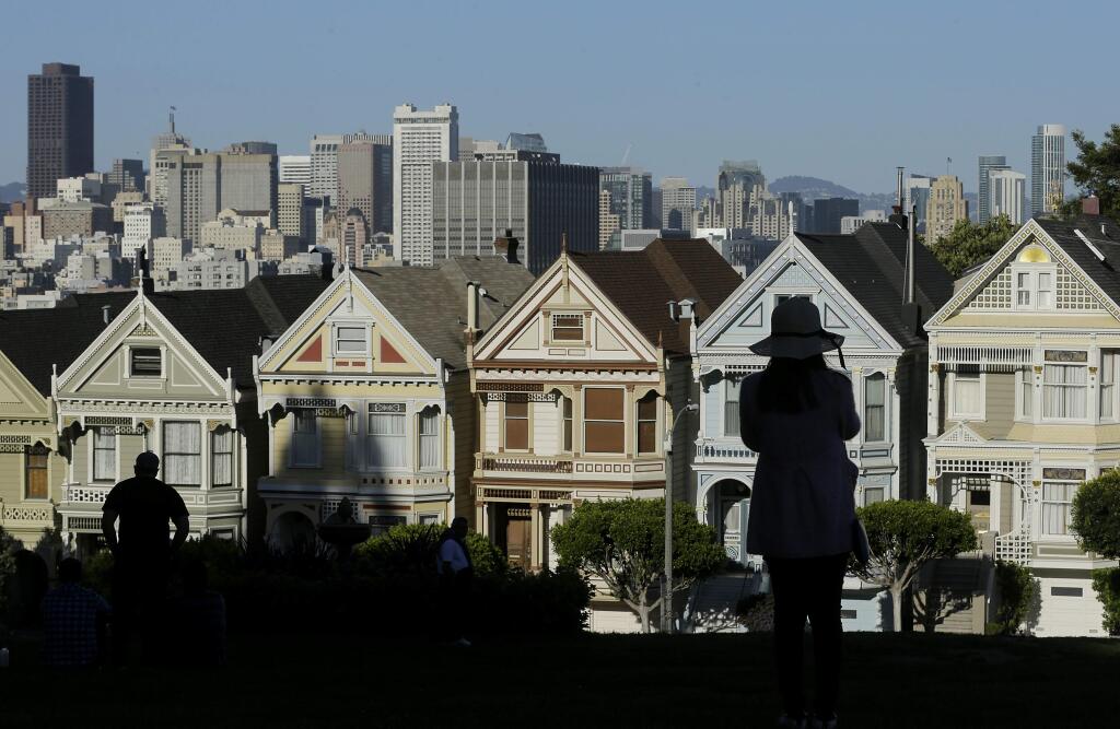 FILE- In this April 15, 2016, file photo a woman looks toward the 'Painted Ladies,' a row of historical Victorian homes, with the San Francisco skyline at rear at Alamo Square Park in San Francisco. The Trump administration announced new rules Thursday, Aug. 23, 2018, aimed at preventing residents in high-tax states from avoiding a new cap on widely popular state and local tax deductions. (AP Photo/Jeff Chiu, File)