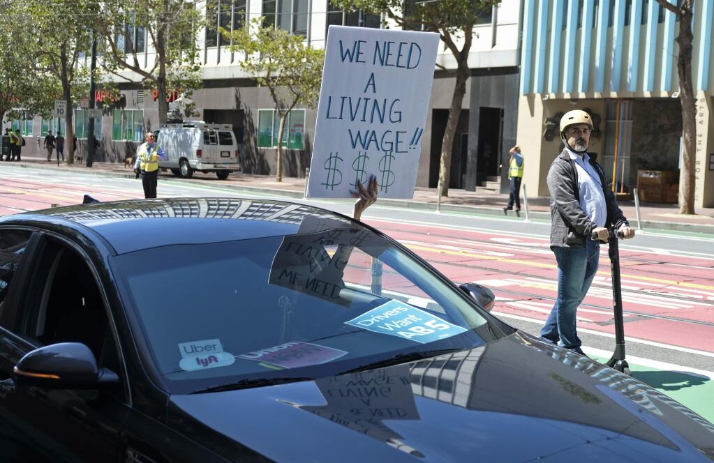 An Uber/Lyft driver holds up a sign while circling the headquarters of Uber during a protest Tuesday, Aug. 27, 2019, in San Francisco. The drivers are seeking to create a union and more basic worker protections. (AP Photo/Eric Risberg)