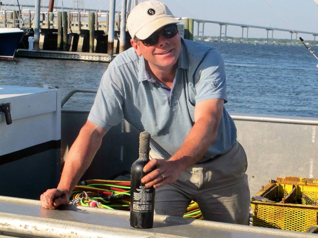 Jim 'Bear' Dyke, the owner of Mira Winery, hands a bottle of wine off a boat docked in Charleston, S.C., on Tuesday, May 6, 2014. The wine had just been recovered after being aged in Charleston Harbor for six months as part of an ongoing experiment by the winery to gauge the effect of ocean aging on wine. Other cases of wine had been aged in the harbor last year for three months. (AP Photo/Bruce Smith)